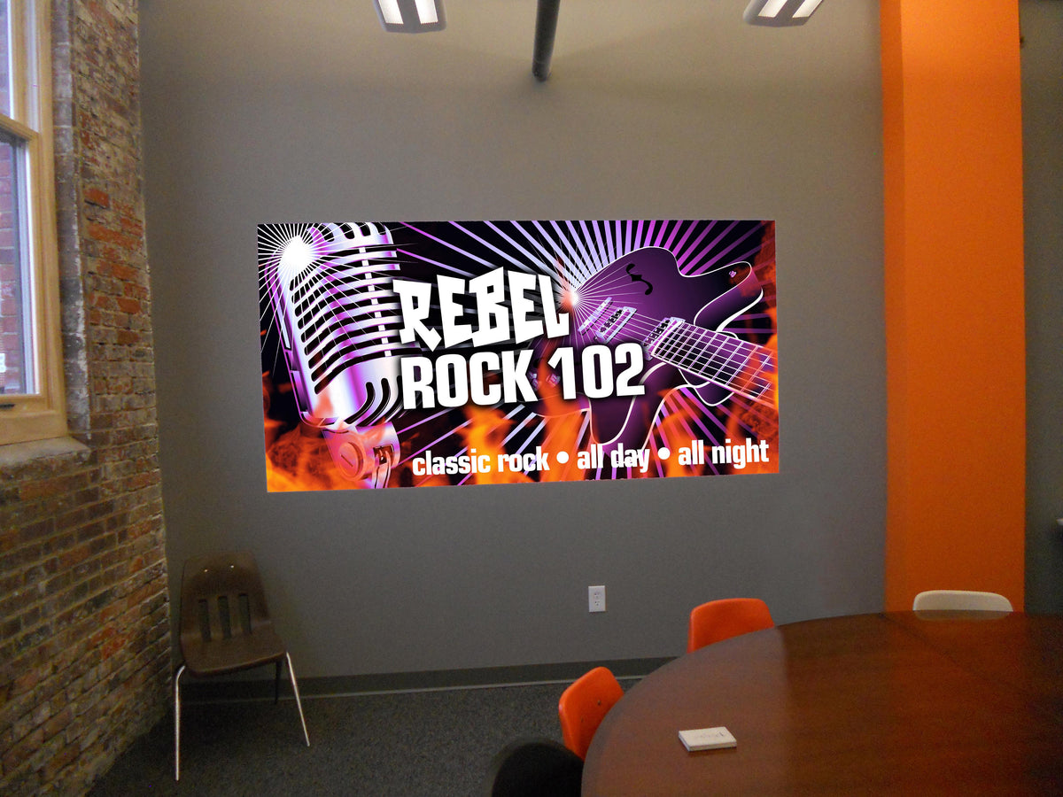A colourful REBEL Rock 102 promotional sign displayed on an interior wall.